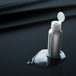 Lubrication - Silver Lube bottle with lube running down the side and puddling on a black fluid proof sheet