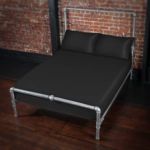 Fluid proof fitted sheet and pillowcases in black on a silver metal bed frame against a brick wall