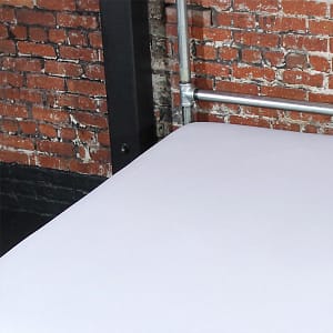 White fluid-proof throw on bed with silver frame against brick wall