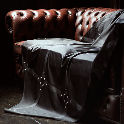 Black Throw printed with black leather straps draped over a red Chesterfield sofa